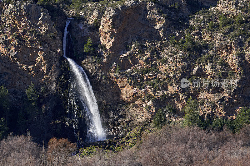 Beautiful landscape near the waterfall near the old town of Domeño on a rocky mountain and leafless trees in the lower part, in Valencia, Spain